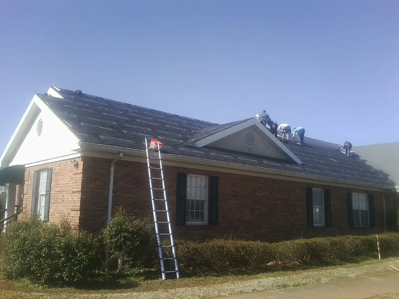 Crew tearing shingles off a brick ranch roof with a ladder set — Emergency Roof Repair work by our crew in Litchfield
