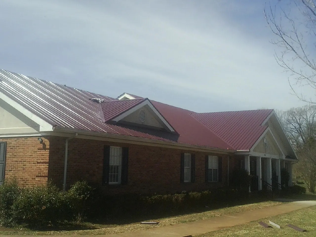 Red metal roof with gabled entries on a long brick building, from a Hail Damage Roof Repair job in Litchfield